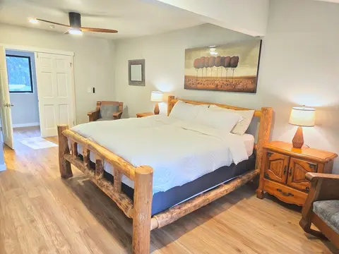 Relax in a spacious bedroom centered around a striking rustic log bed with crisp, clean linens. Beautiful floors, warm bedside lamps, cozy seating, and a ceiling fan complete this comfortable and inviting retreat.